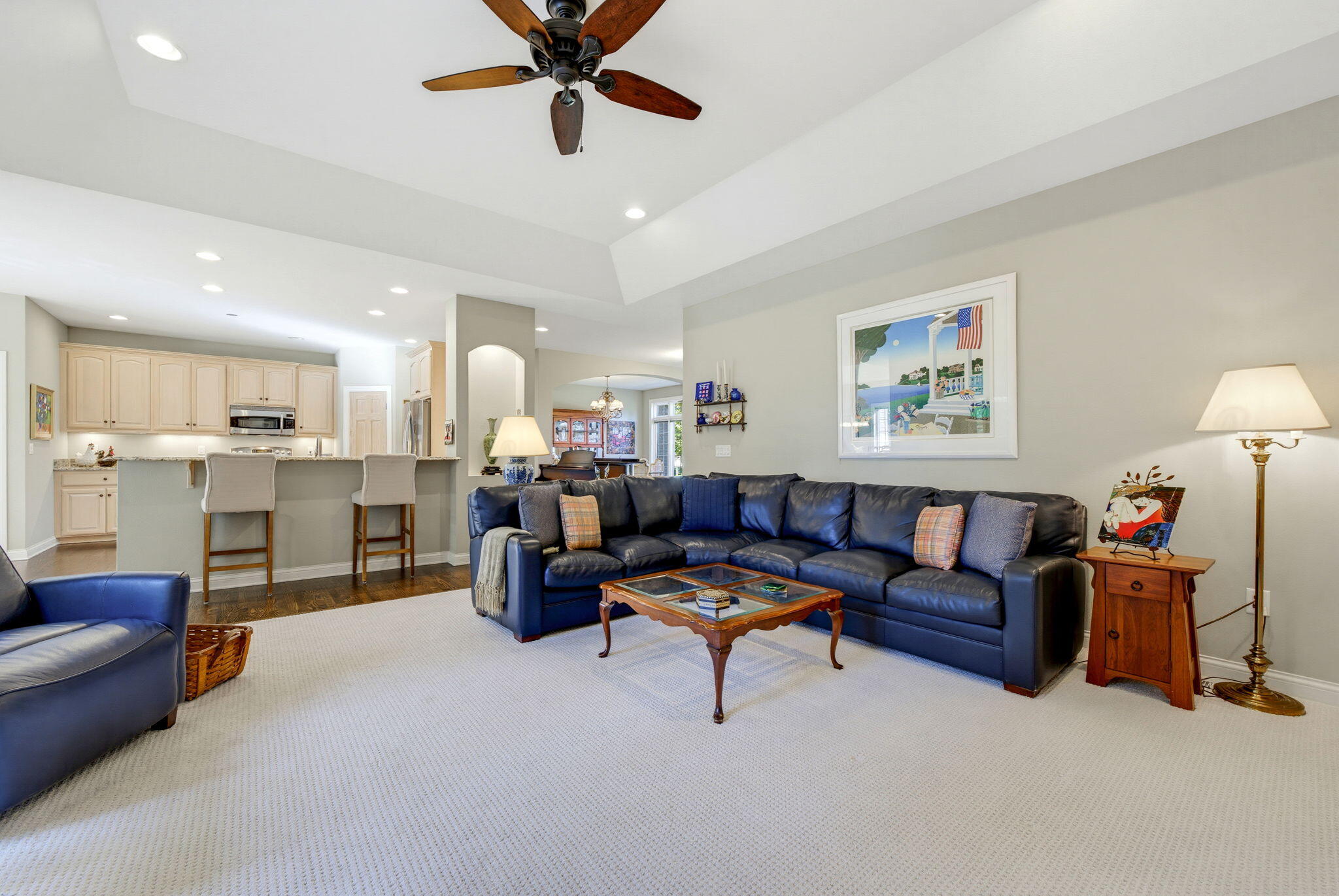 Furnished living room with a dark blue sectional, wood coffee table, and open kitchen with breakfast bar.