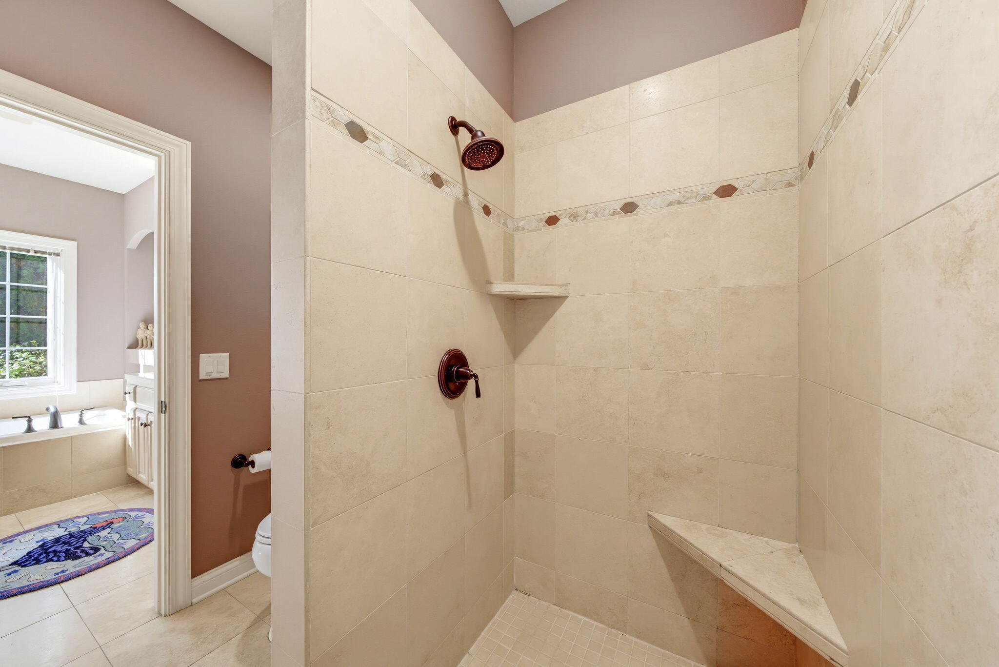 Walk-in tiled shower with a mosaic border, bronze fixtures, and a built-in corner seat.