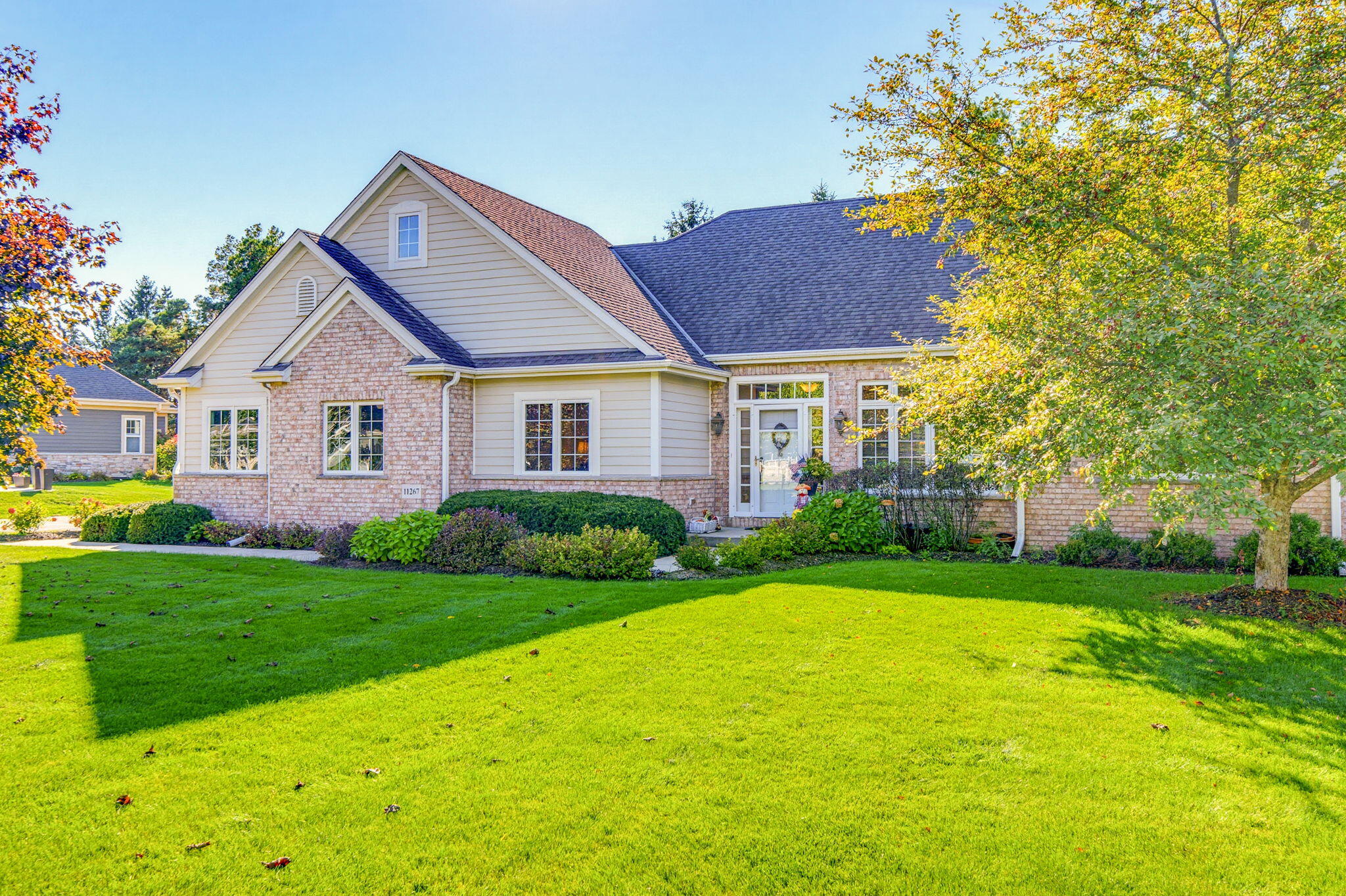 Home exterior with brick accents, a broad green lawn, and mature autumn trees.