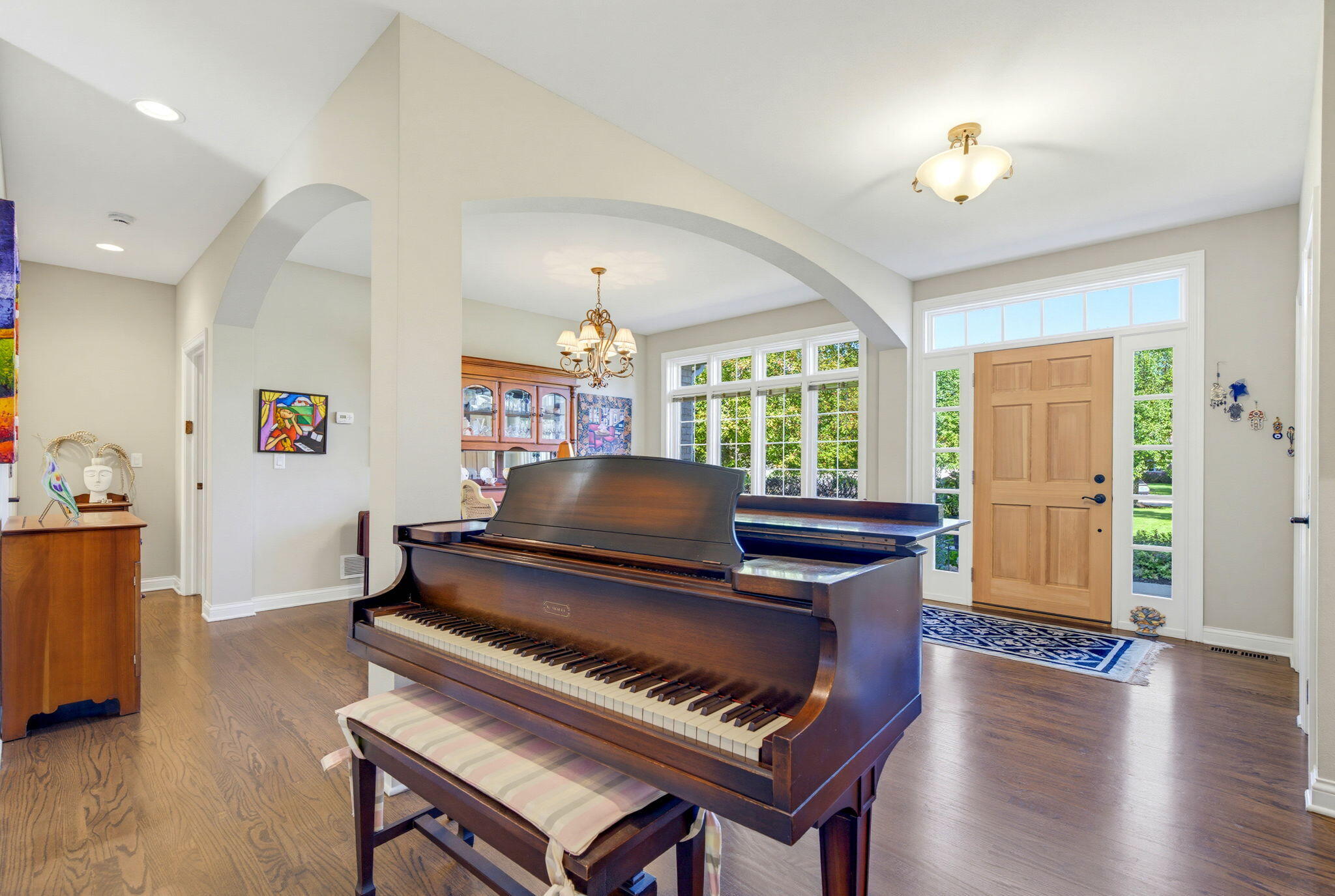 Entry hall with a grand piano, hardwood floors, and a front door with glass sidelights.