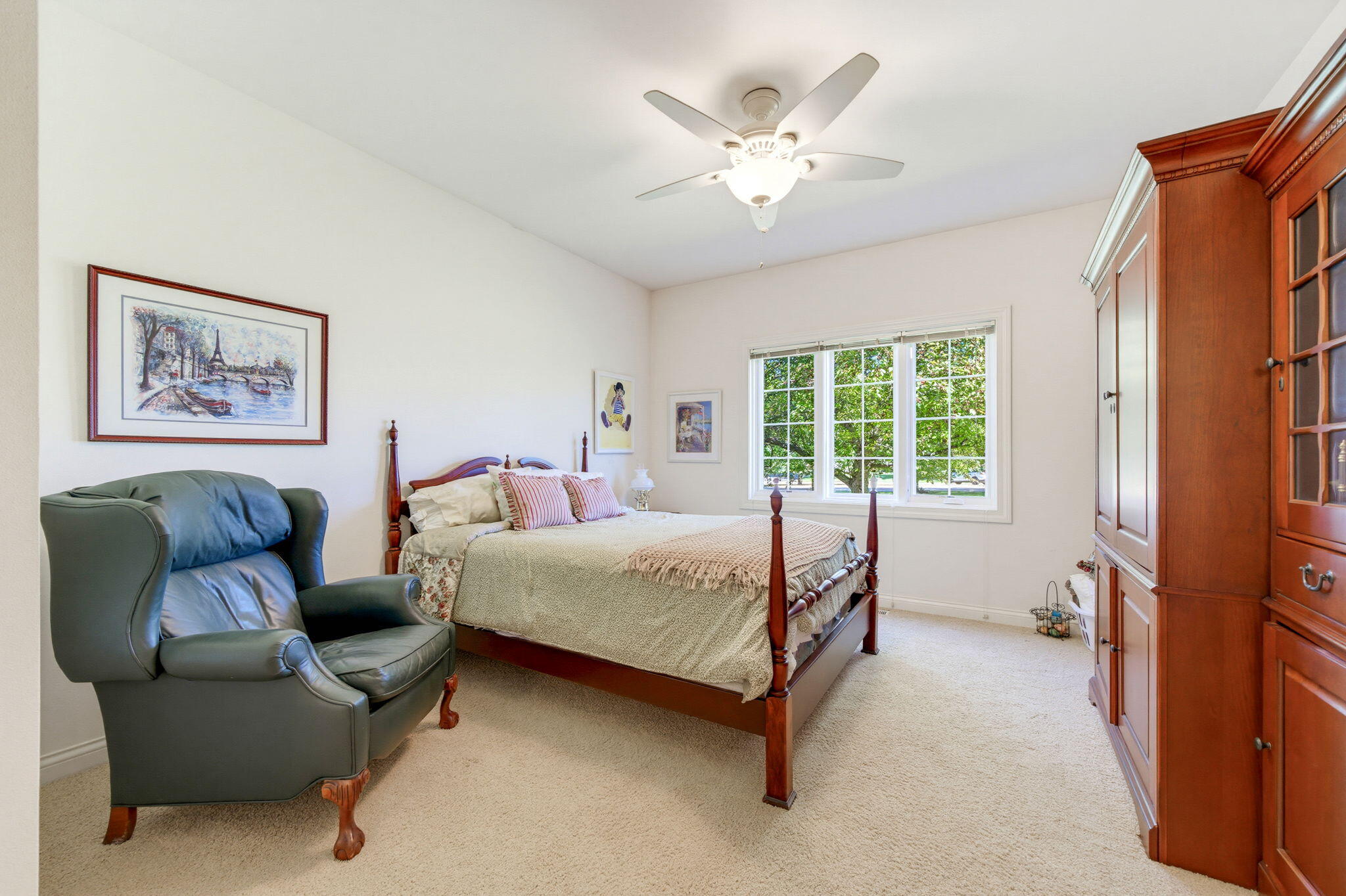 Bedroom with a four-poster bed, green leather armchair, and built-in wood cabinetry beside a sunny window.