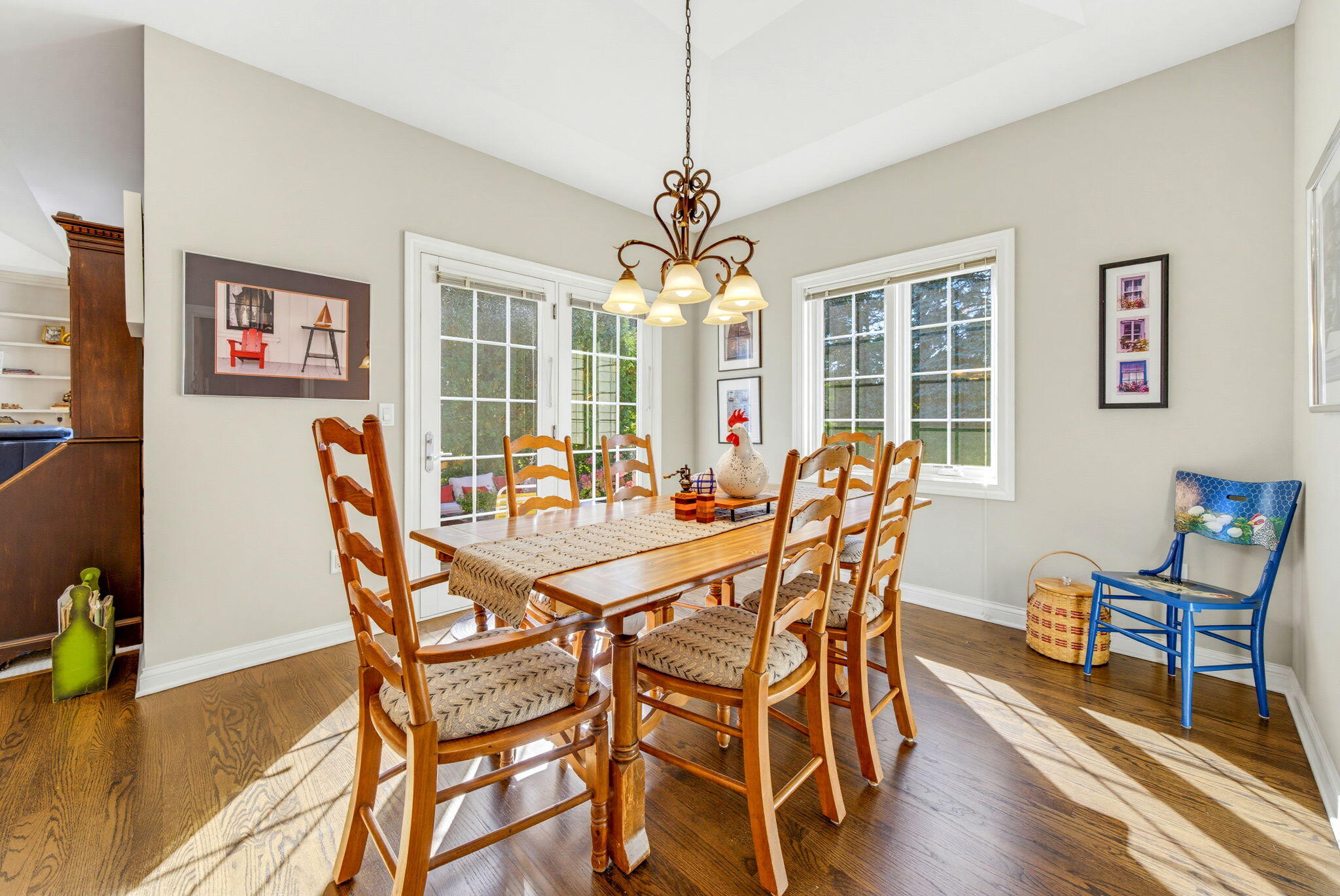 Dining room with a wooden table, decorative chandelier, hardwood floors, and large windows.