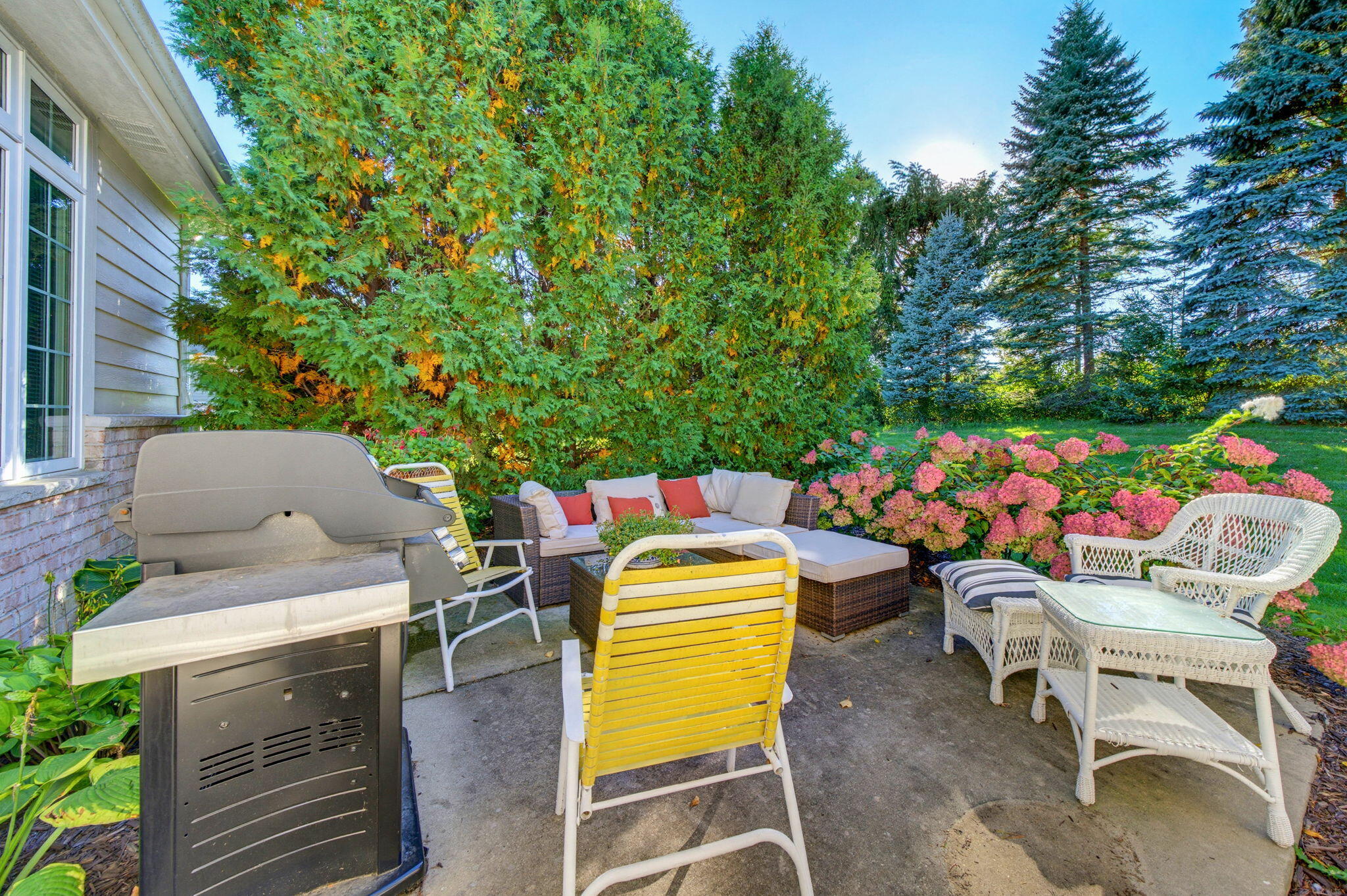 Patio with a grill, cushioned seating, white wicker chairs, and pink hydrangeas.