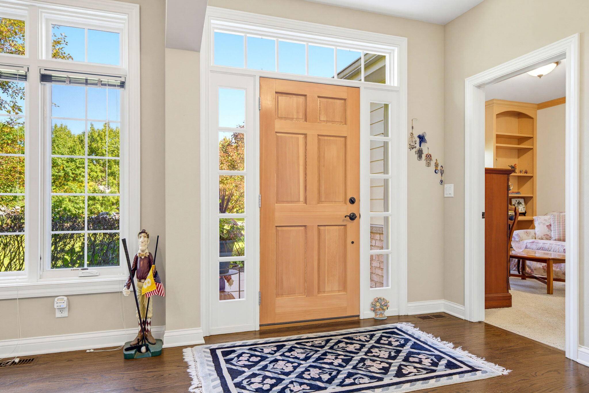 Entry foyer with a paneled wood front door, tall windows, hardwood floors, and a patterned navy rug.