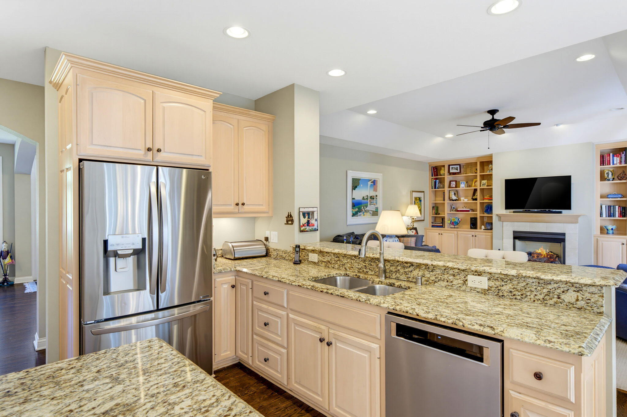 Open-plan kitchen with pale wood cabinets, granite counters, stainless appliances, and a view of the living room.