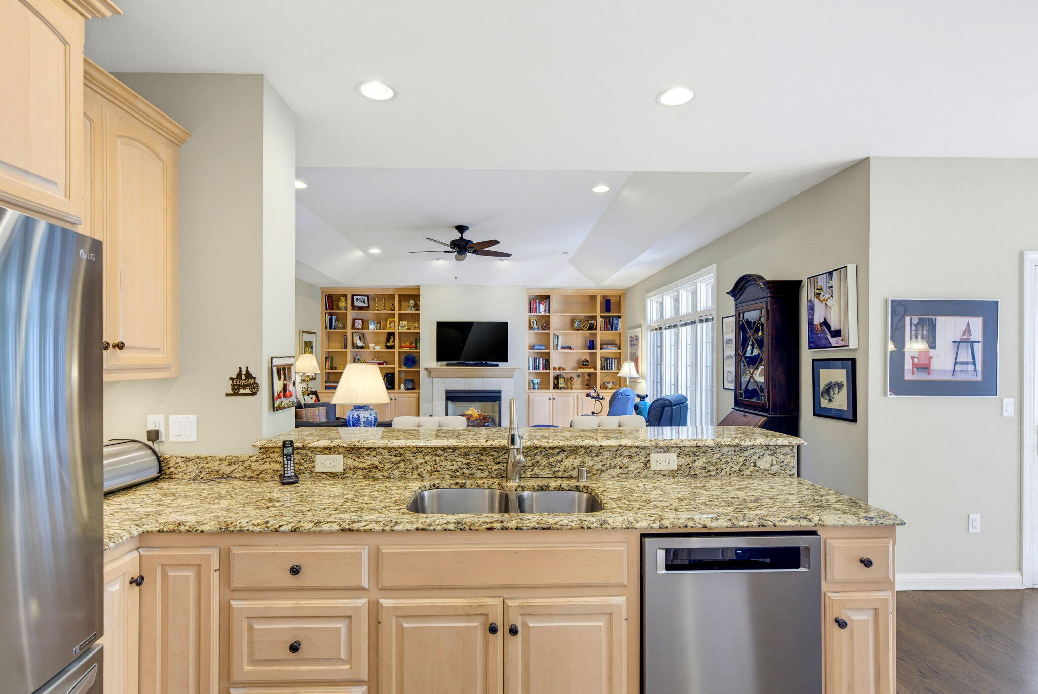 Kitchen with light wood cabinetry and granite counters overlooking a living room with built-ins and a fireplace.