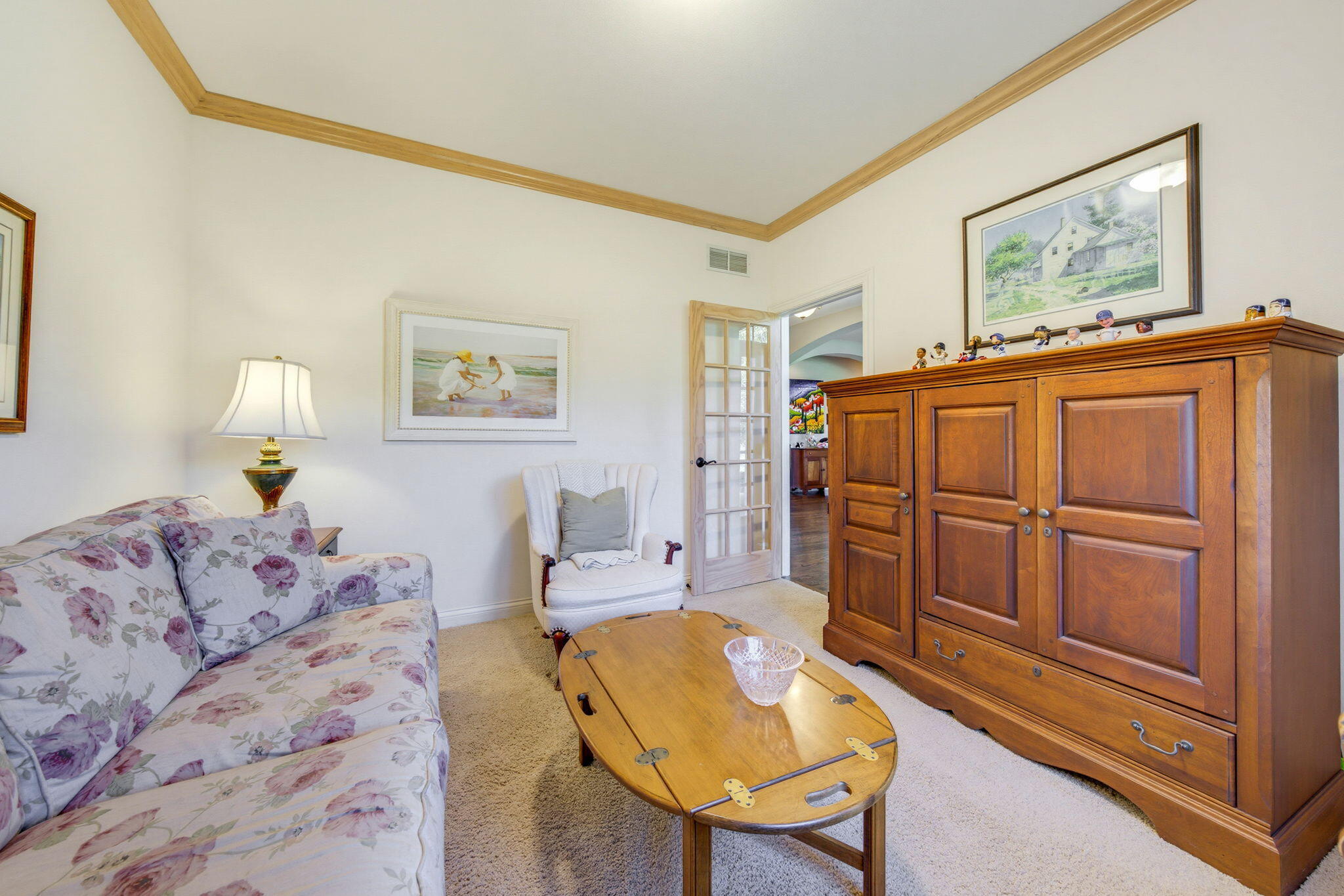 Sitting room with floral sofa, white armchair, and large wooden armoire