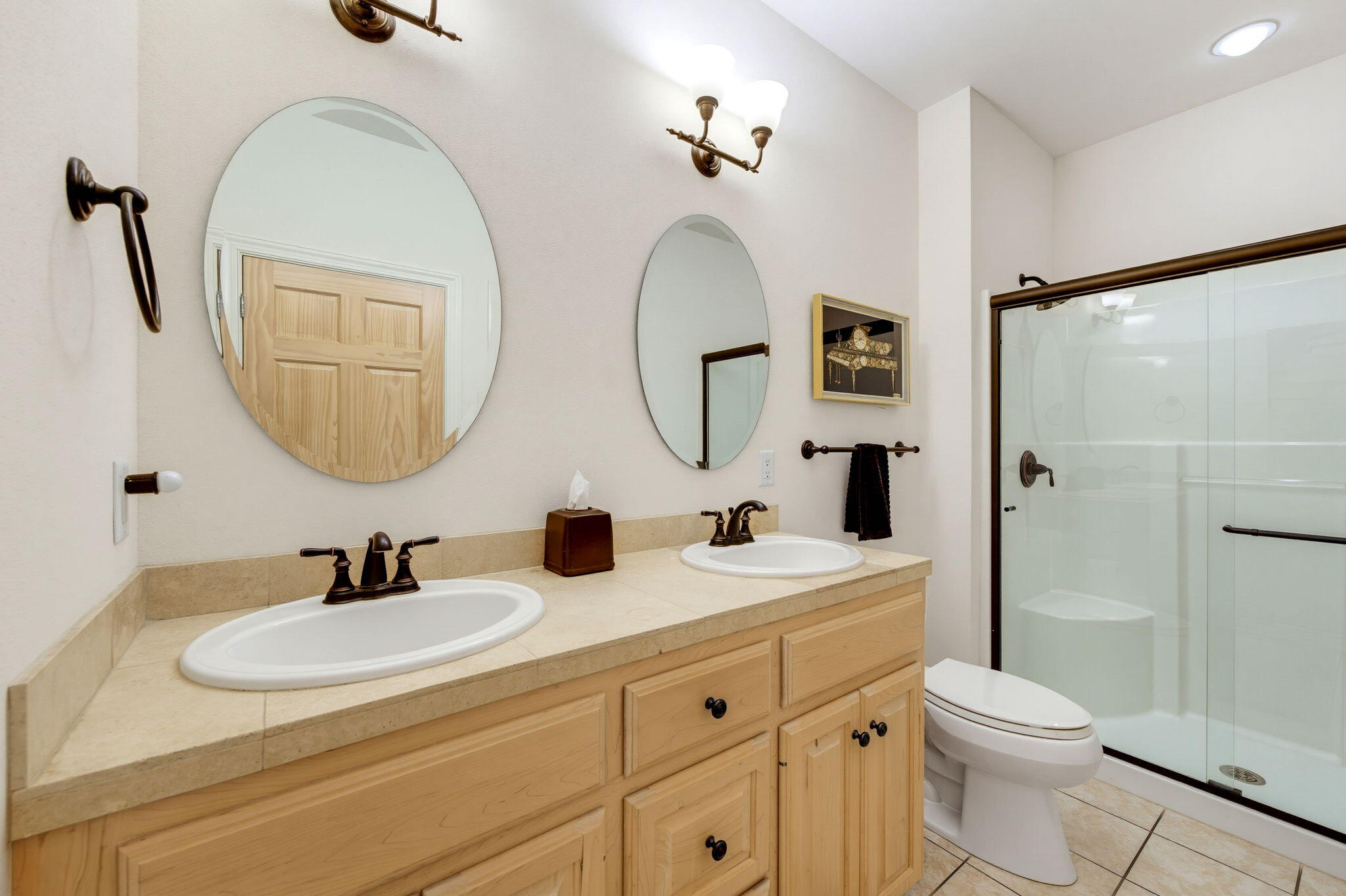 Bathroom with a double-sink wood vanity, oval mirrors, and a glass-enclosed shower.