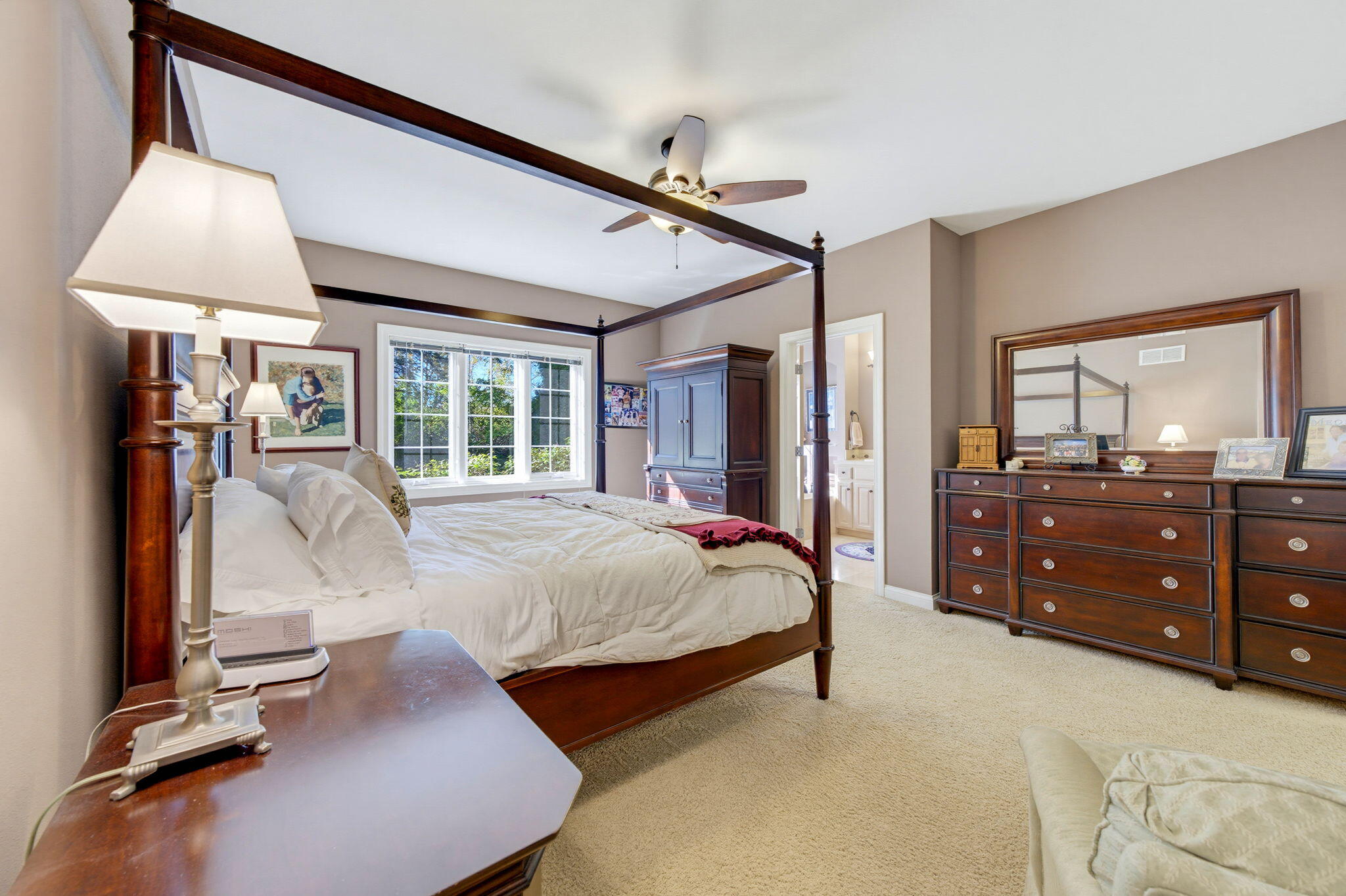 Furnished bedroom with a dark wood four-poster bed, matching dresser, and large daylight-filled window.