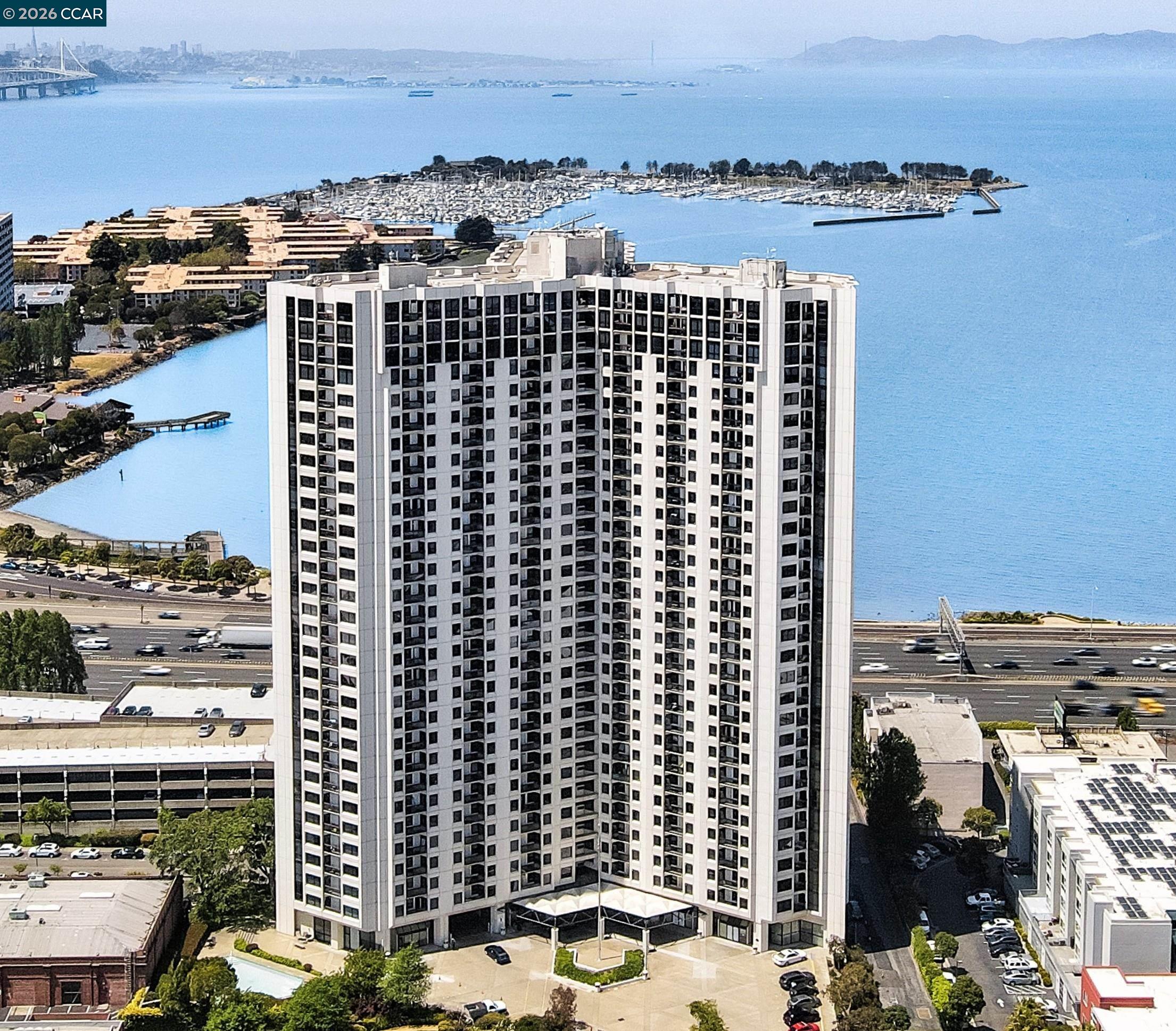 White high-rise condominium beside a bay, with a marina and small pool.