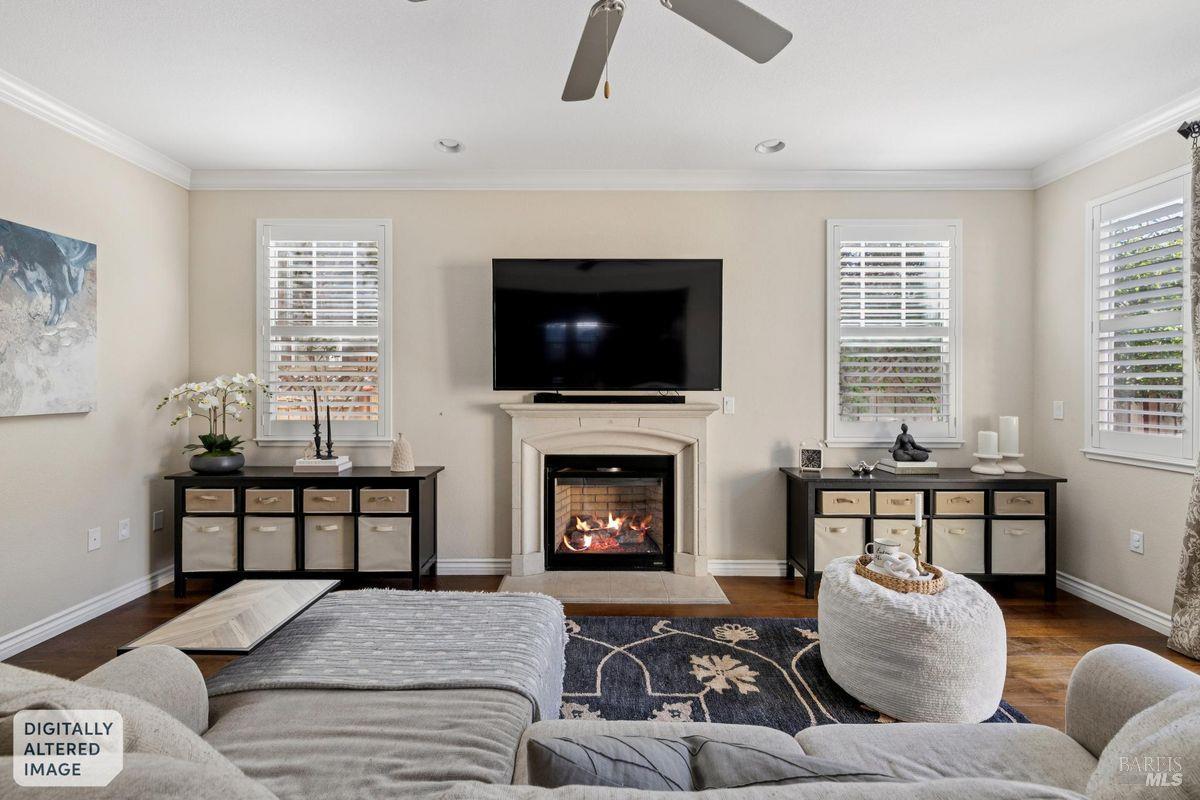 Furnished living room with a lit fireplace, television, shuttered windows, and neutral seating.