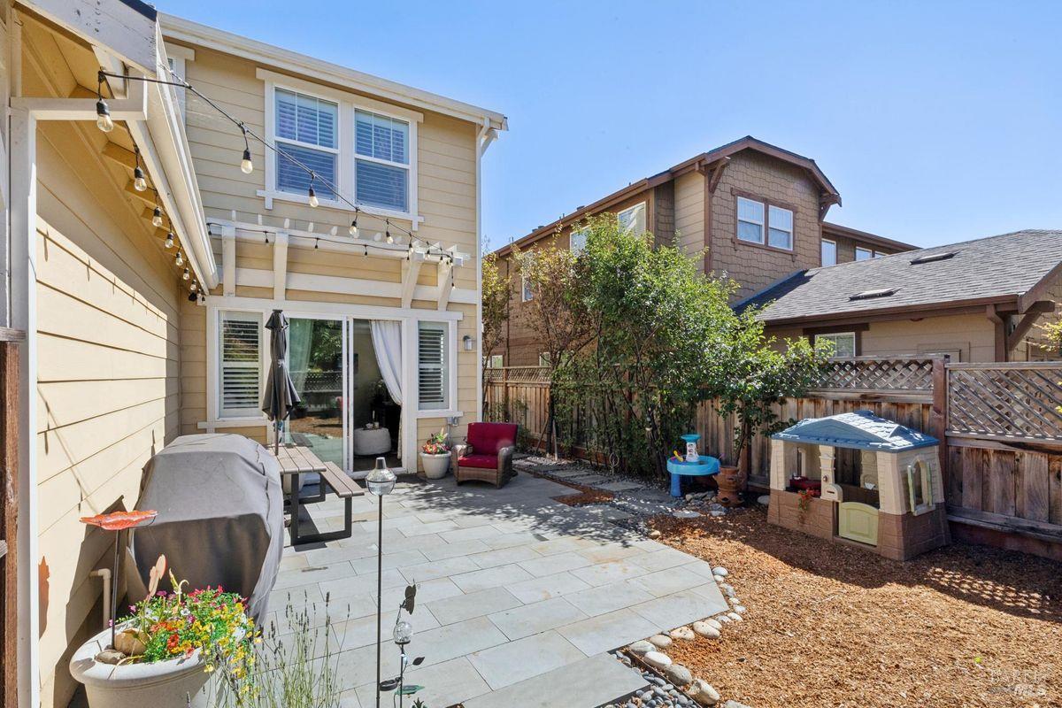 Backyard patio with outdoor seating, string lights, and a children's playhouse.