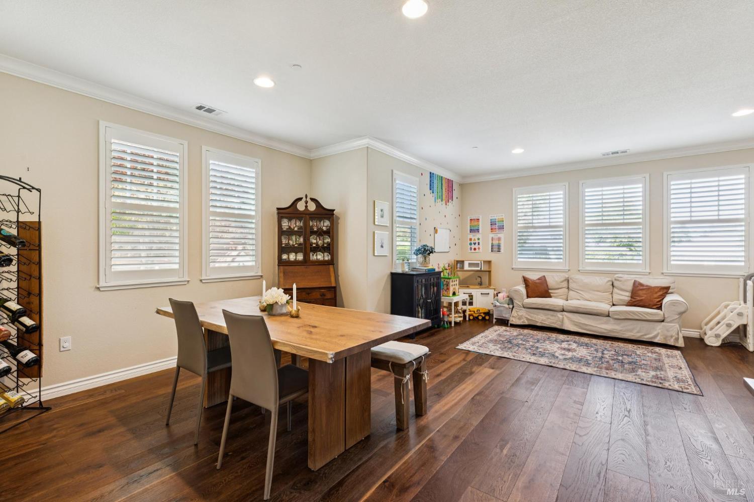 Open-plan dining and living room with hardwood floors, plantation shutters, and a children’s play area.