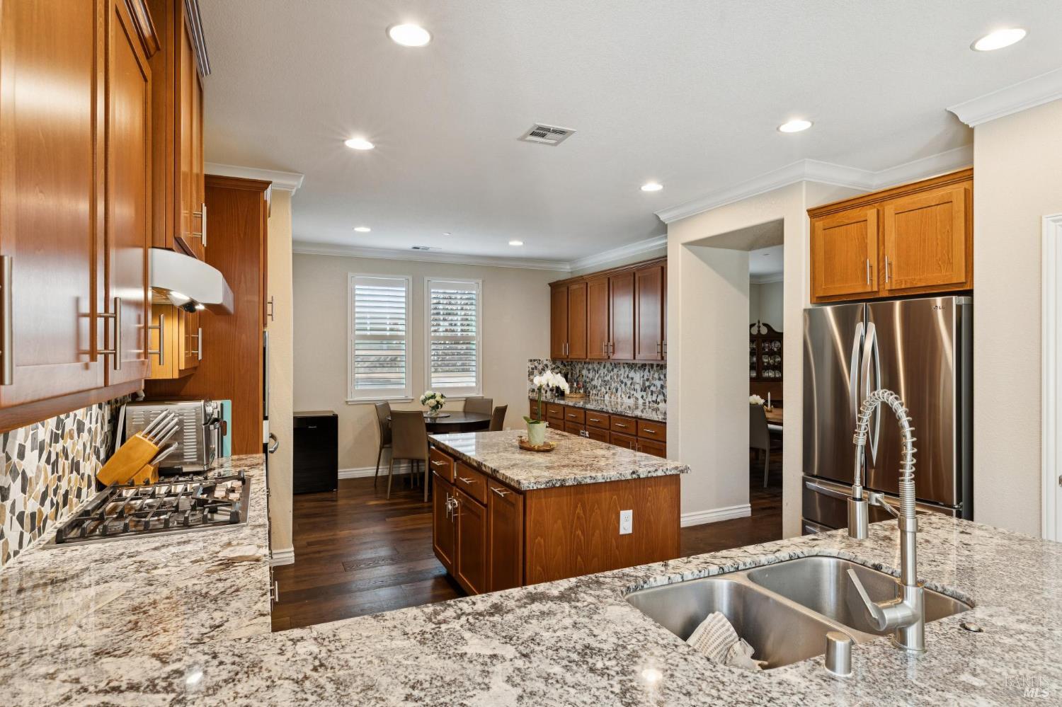 Kitchen with warm wood cabinetry, granite island, stainless steel appliances, and a mosaic tile backsplash.