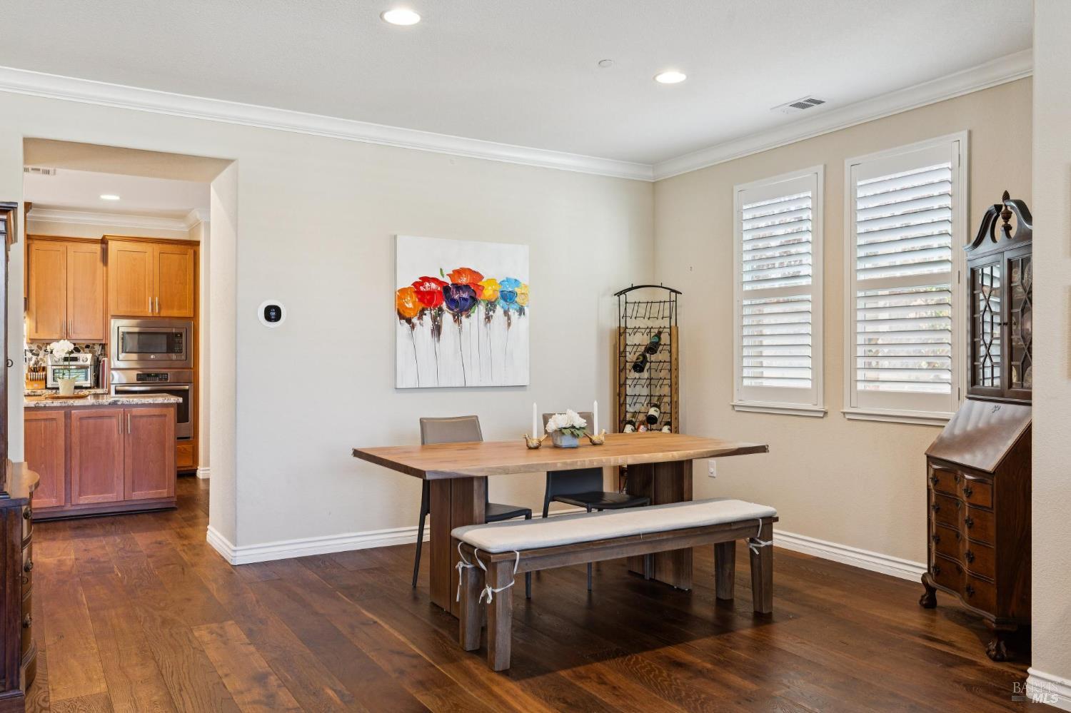 Dining room with a long wooden table, bench, hardwood floors, and white plantation shutters.