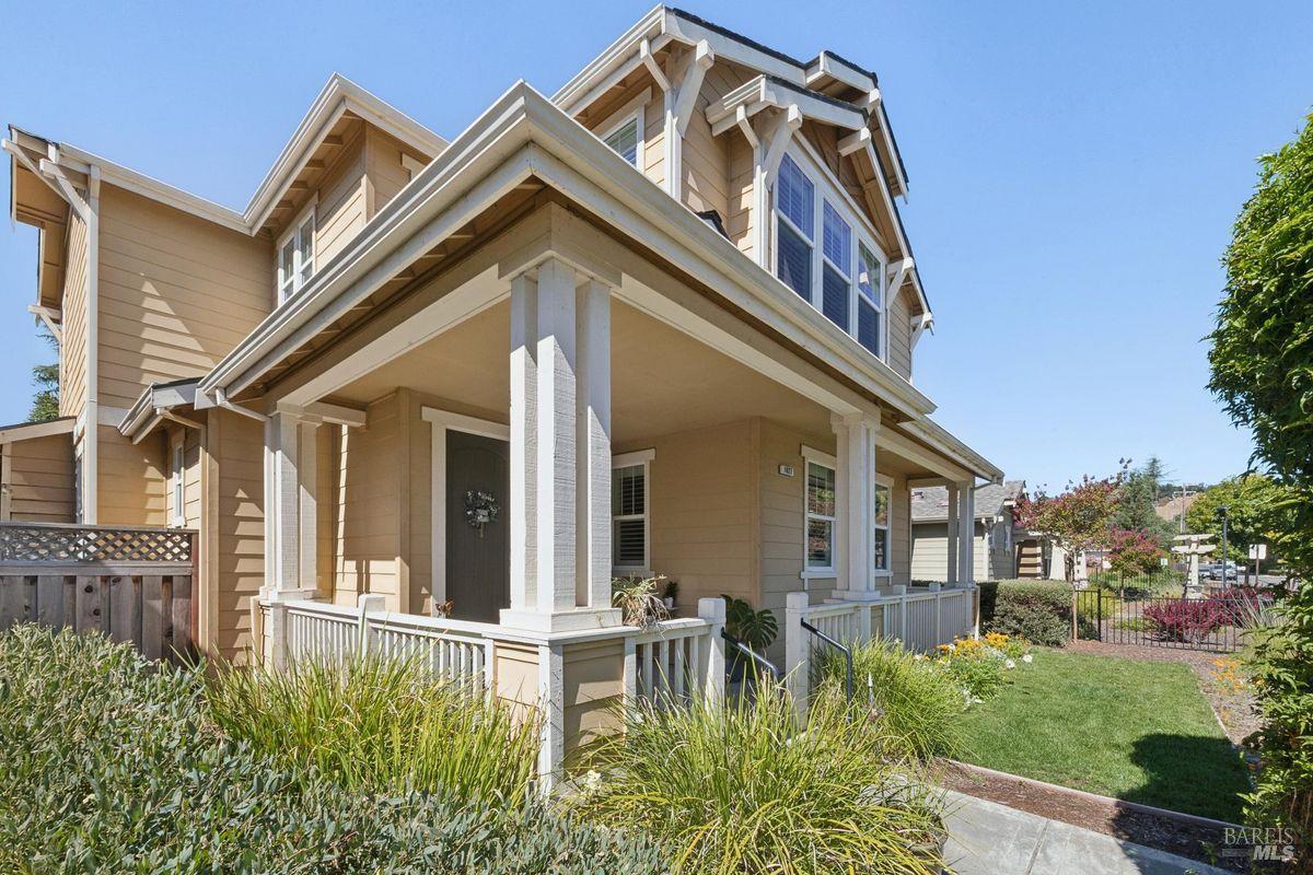 Tan multi-story house with a covered white-trimmed porch and landscaped front yard.