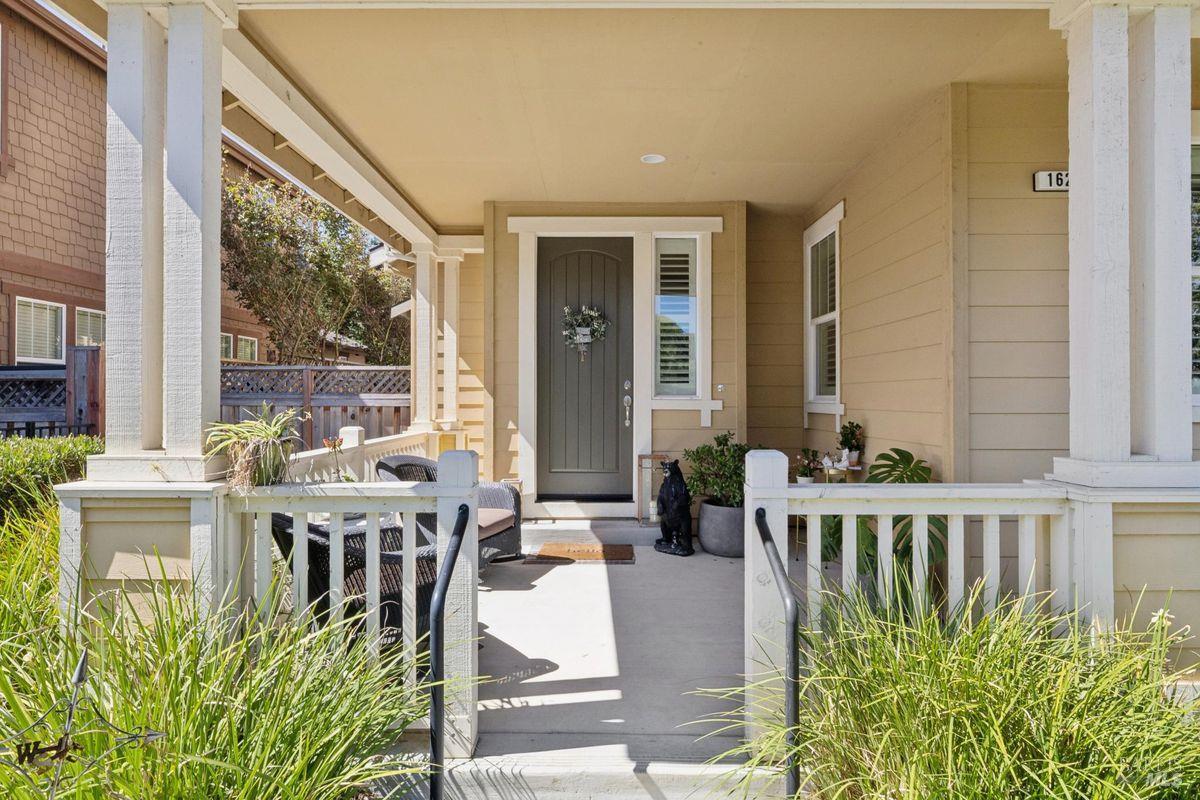 Home’s covered front porch with a gray door, white railings, seating, and potted plants.