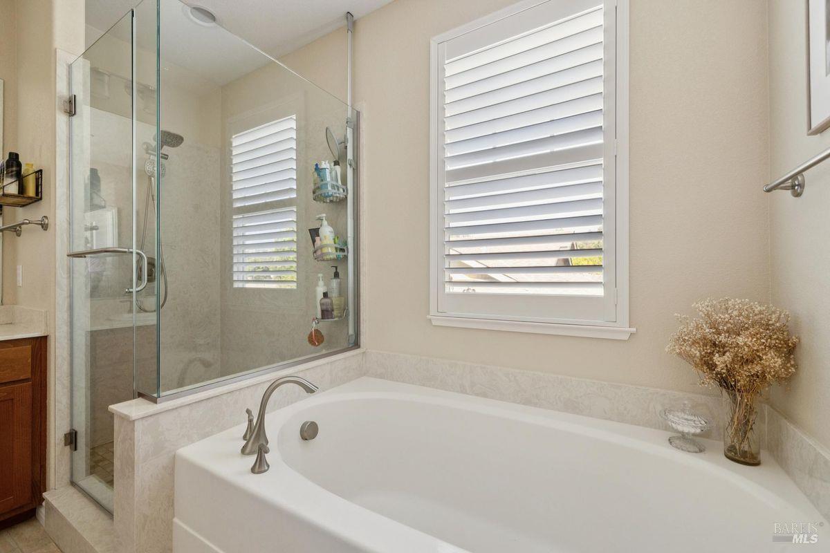 Bathroom with a glass-enclosed shower, soaking tub, and white plantation shutters.