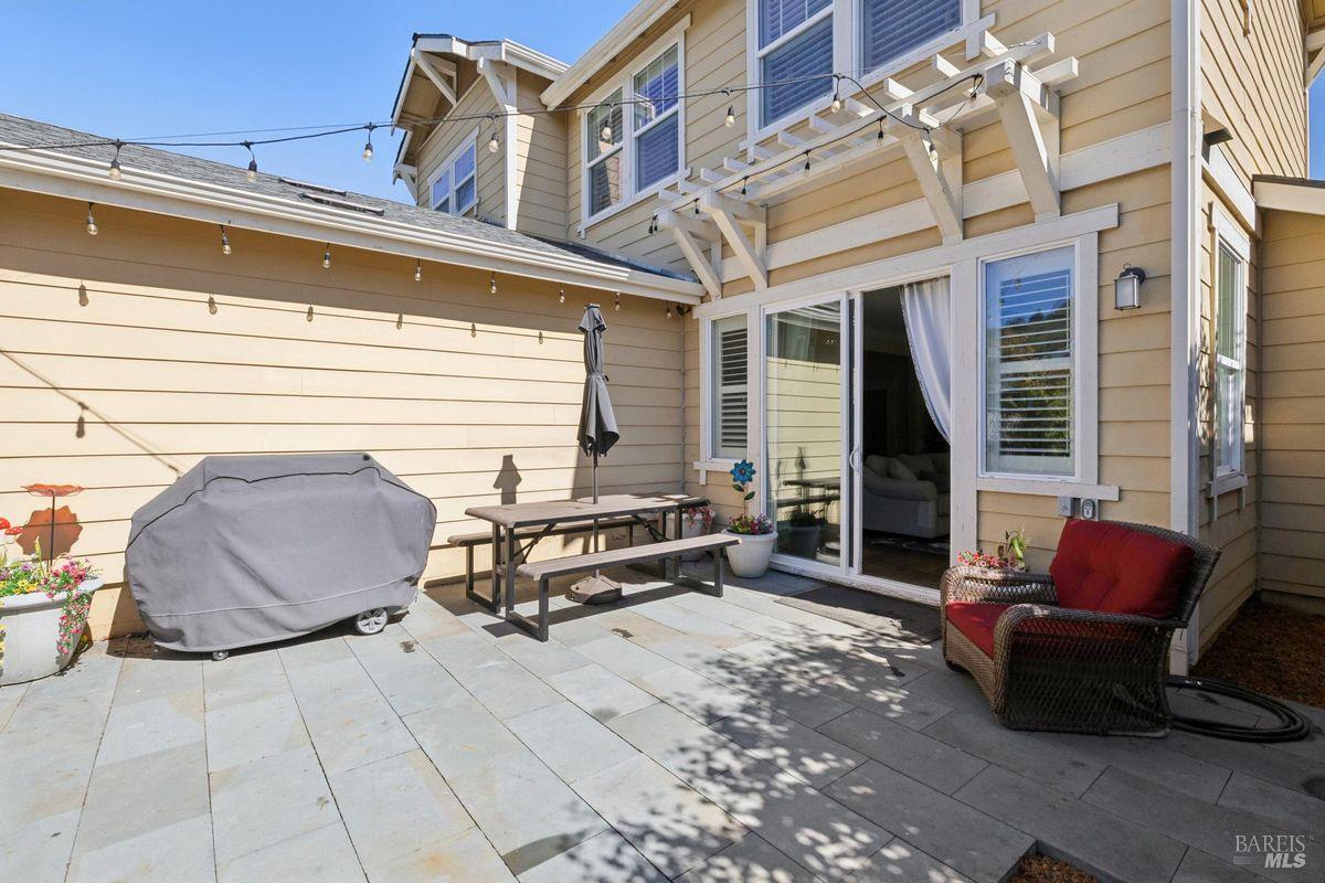 Backyard patio with a white pergola, string lights, and sliding glass doors.