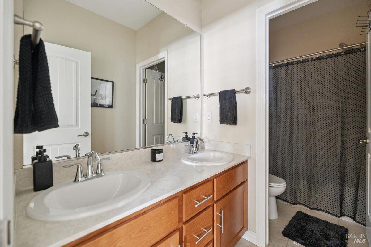 Bathroom with a long double-sink vanity, wood cabinetry, and a curtained shower.