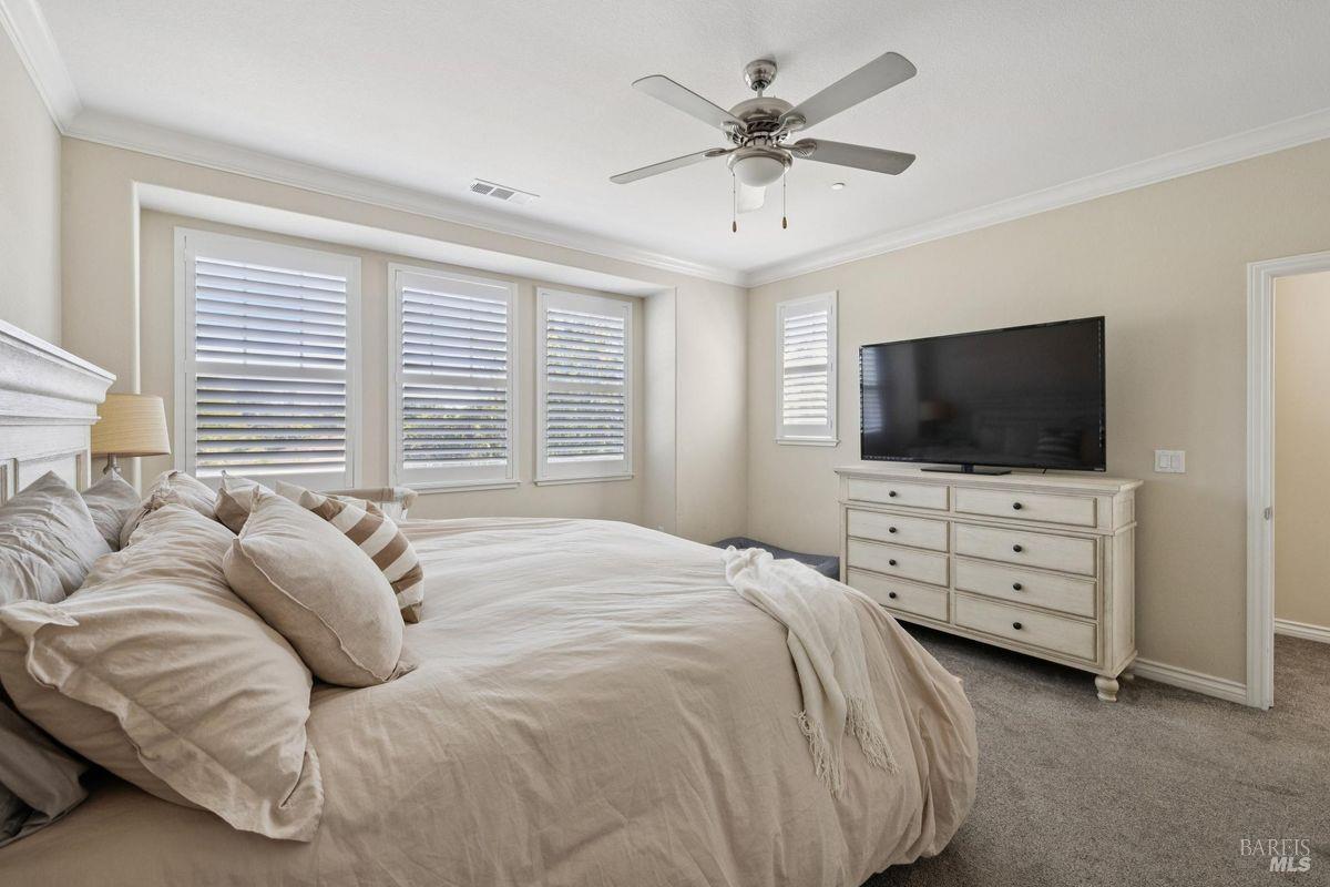 Bedroom with a large neutral-toned bed, shuttered windows, and a television on a dresser.
