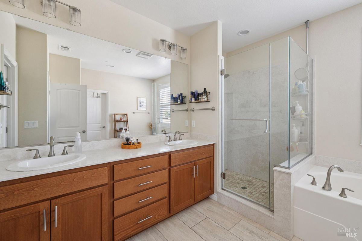 Primary bathroom with double wood vanity, glass shower, and soaking tub.
