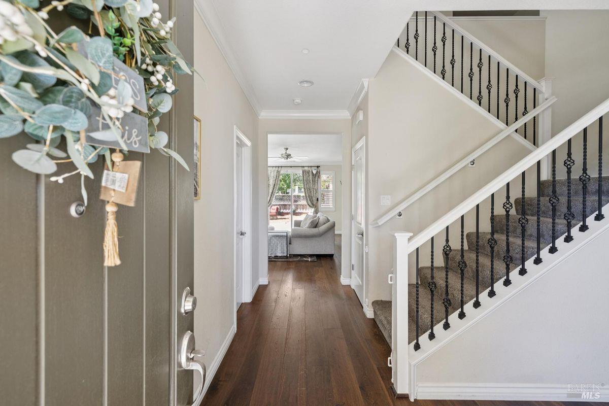 Entryway with a hardwood hallway, dark front door, and staircase with black iron balusters.