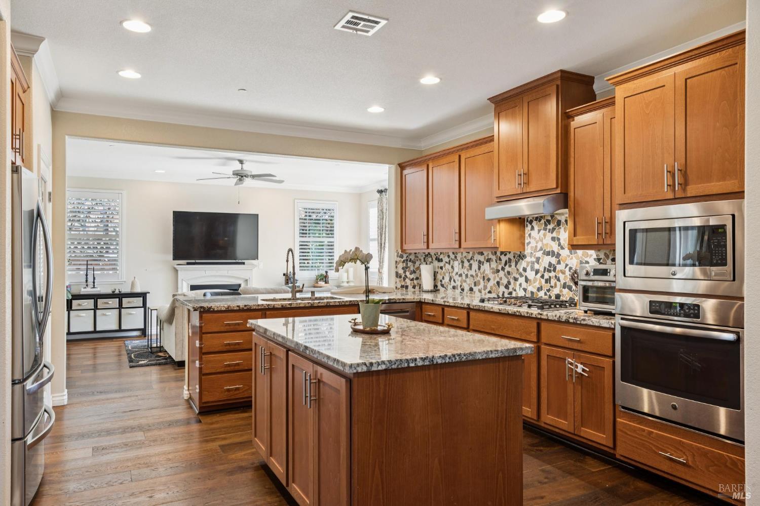 Kitchen with wood cabinets, granite island, mosaic backsplash, and stainless steel appliances, opening to the living room.