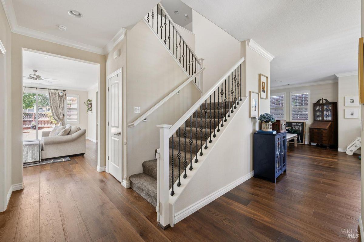 Entry foyer with a carpeted staircase and black iron balusters, hardwood floors, and adjoining furnished rooms.