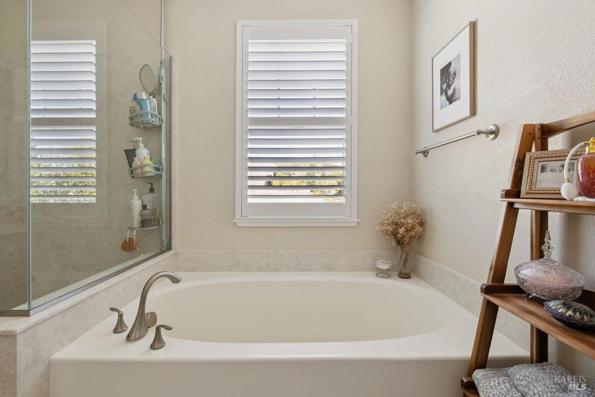 Bathroom with a built-in soaking tub, glass shower enclosure, and white plantation shutters.