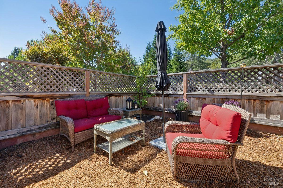 Outdoor patio with red-cushioned wicker seating, a glass-topped table, and a closed umbrella.