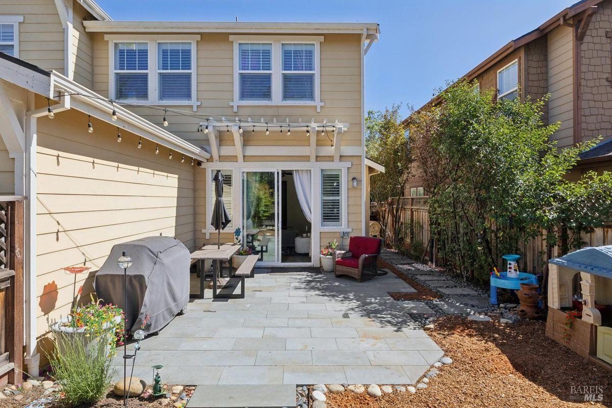 Backyard patio with a paved terrace, outdoor dining set, covered grill, and string lights.