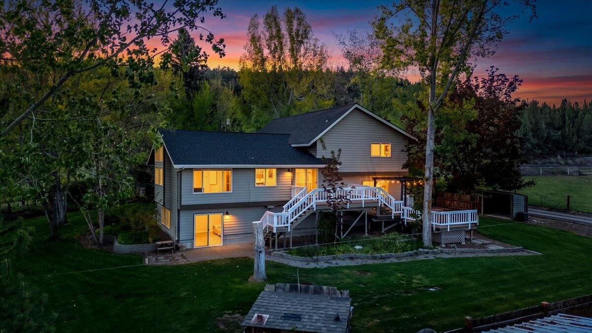 Two-story gray home with a white-railed deck and glowing windows at dusk.