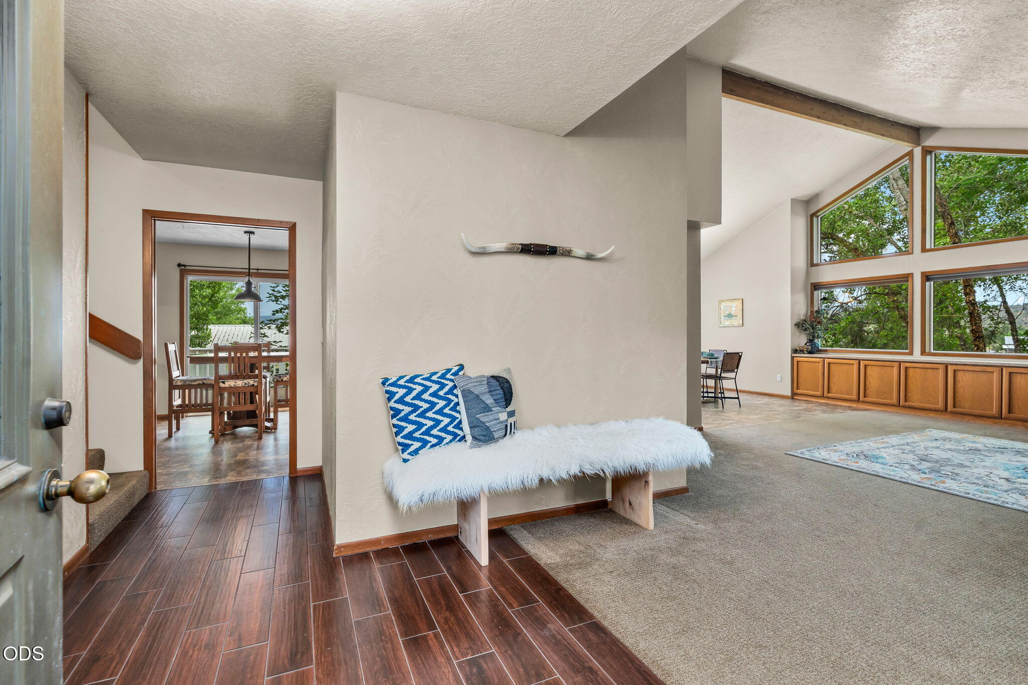 Entry opens to a bright living room with a fur-covered bench, large windows, and built-in wood cabinets.