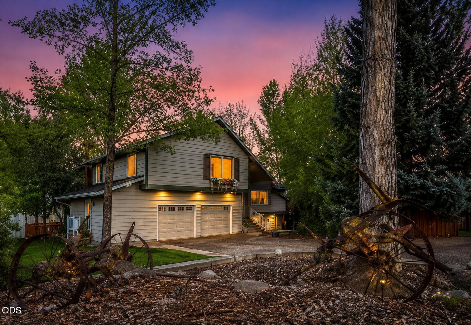 Two-story gray house with lit windows and double garage, framed by trees at dusk.