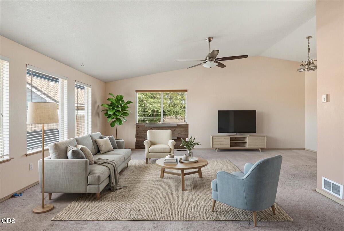 Staged living room with a vaulted ceiling, large windows, gray sofa, and television.
