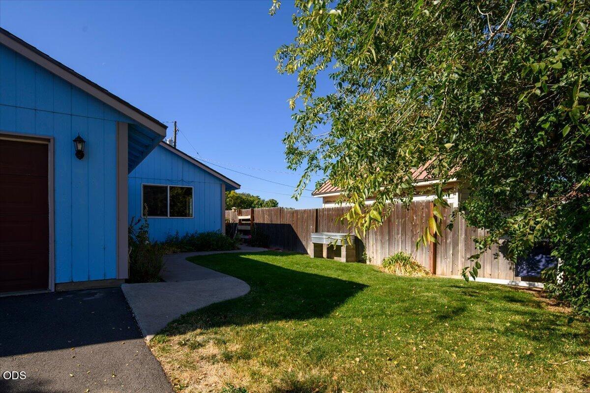Backyard with blue outbuilding, curved concrete walkway, lawn, and wooden privacy fence.