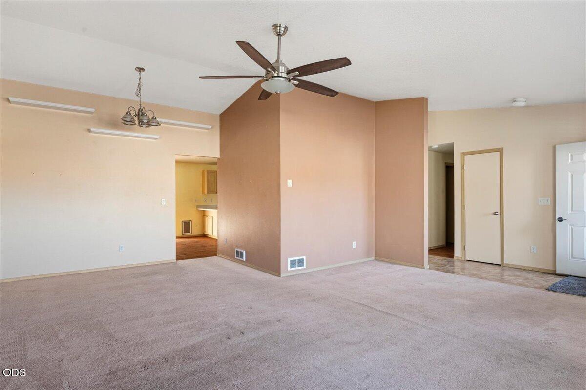 Empty living room with beige carpet, terracotta accent walls, and a ceiling fan.