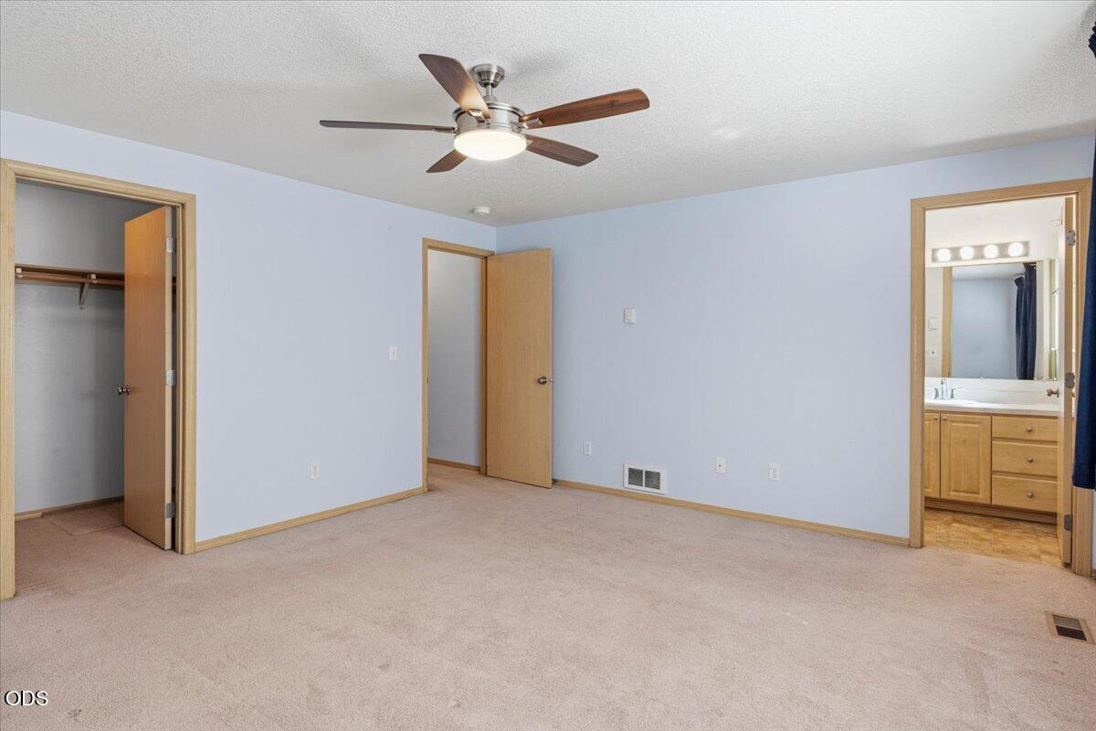 Vacant bedroom with a ceiling fan, open closet, and adjoining bathroom vanity.