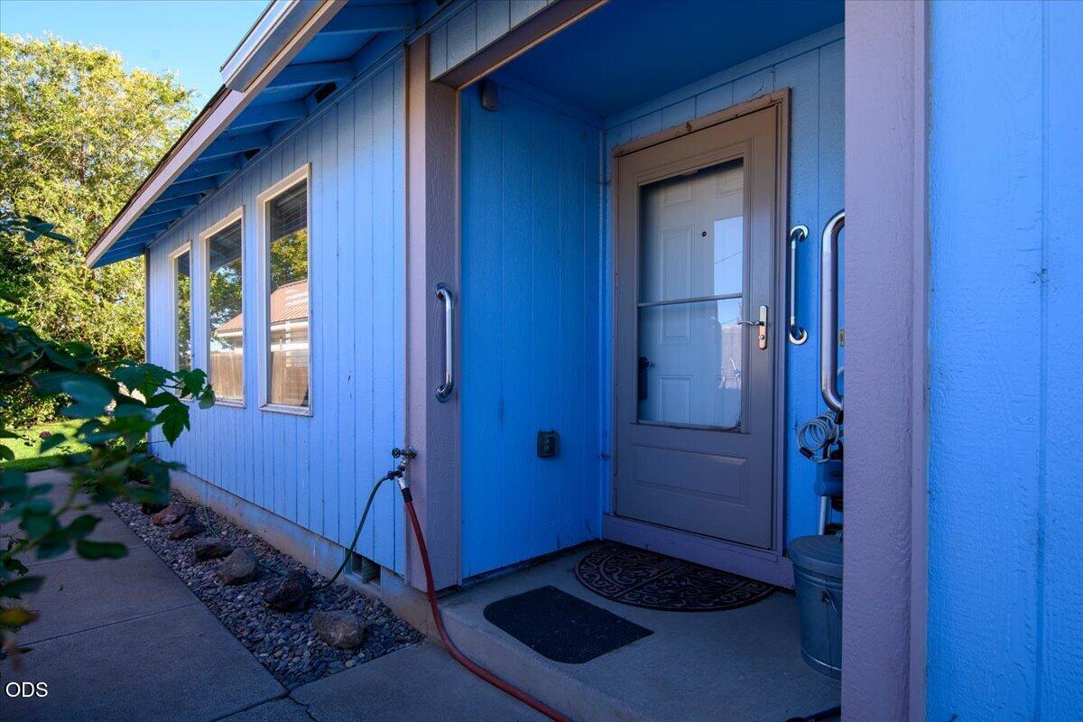 Blue-sided home’s recessed front entry with gray screen door, white-trimmed windows, and rock landscaping.