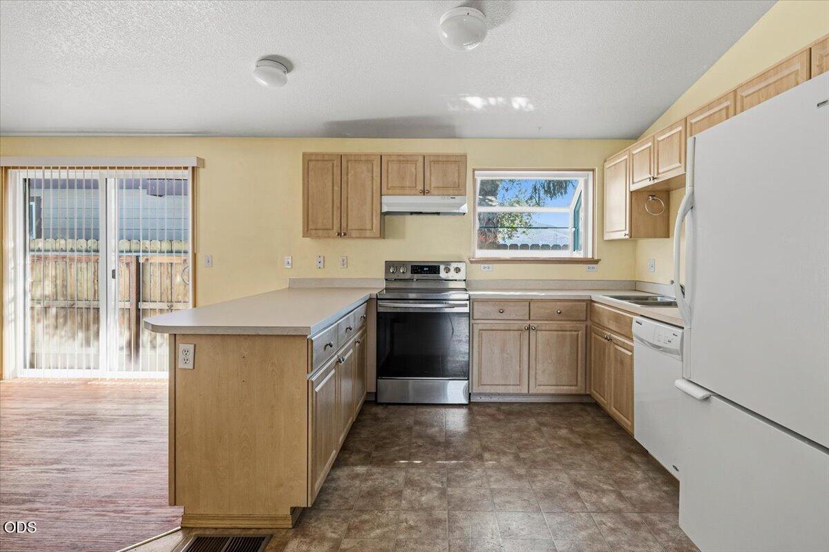 Kitchen with light wood cabinets, a peninsula island, stainless steel range, and sliding glass doors.