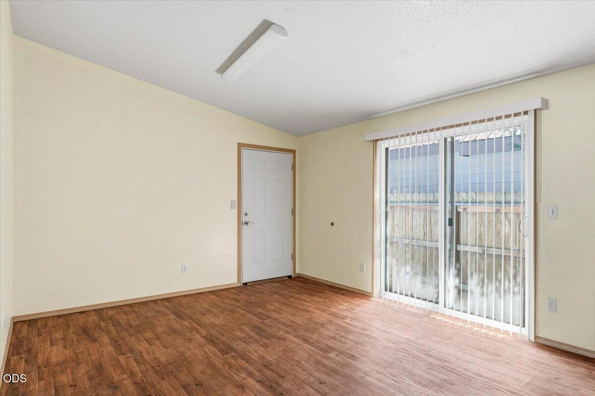 Vacant room with wood-look flooring and sliding glass doors with vertical blinds.