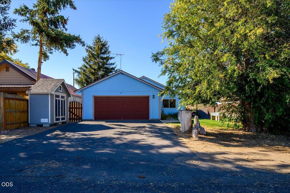 Blue house with a wide reddish-brown garage door, paved driveway, and mature trees.