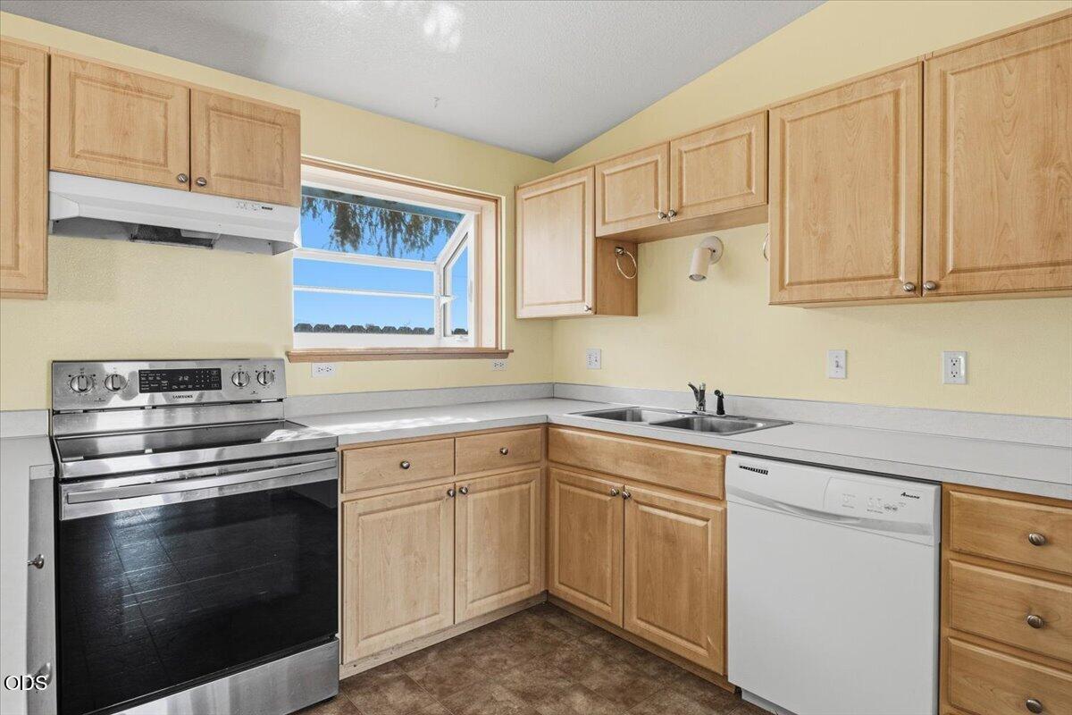Kitchen with light wood cabinets, stainless steel range, and a window above the counter.