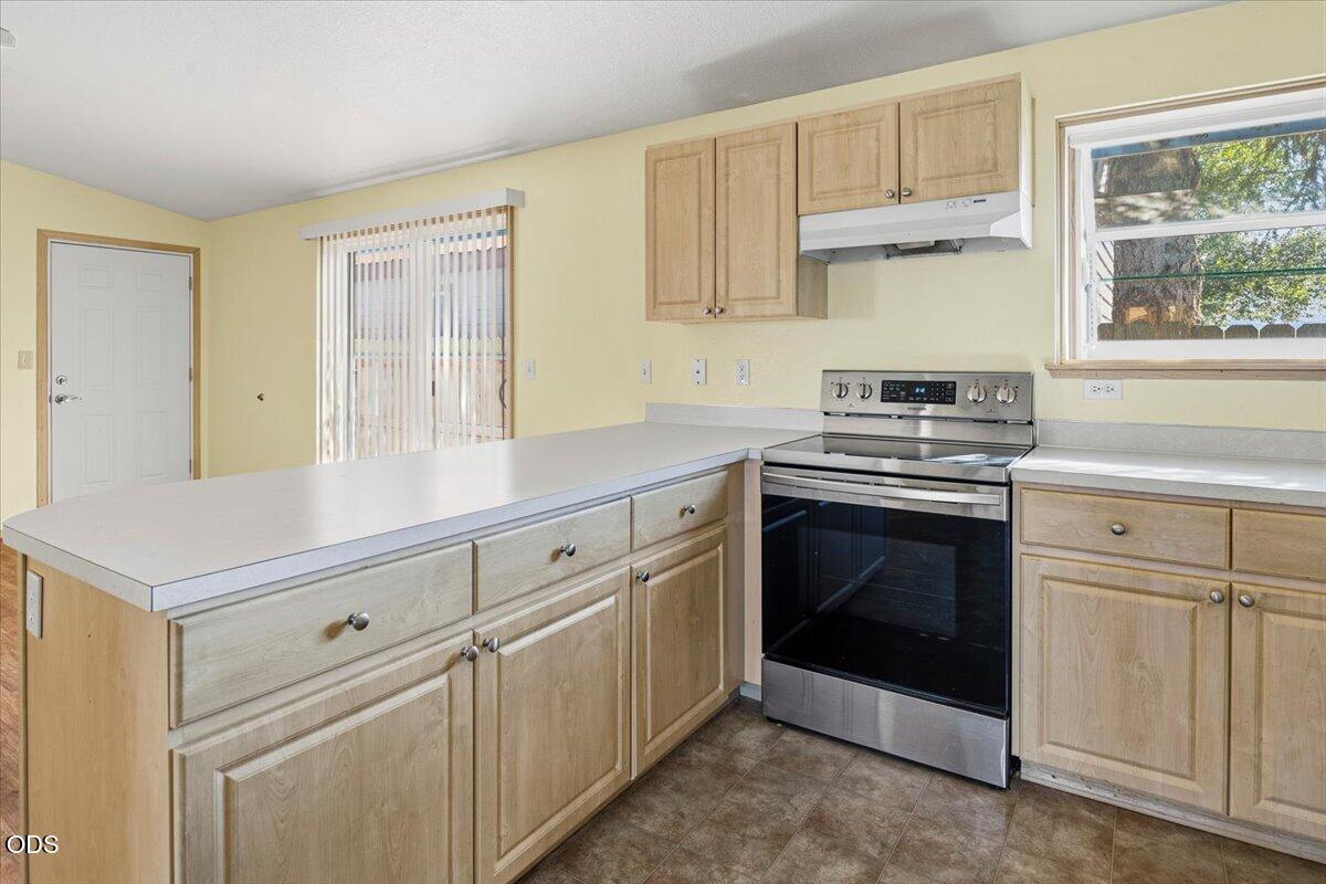 Kitchen with light wood cabinets, a white-countertop peninsula, and a stainless steel range.