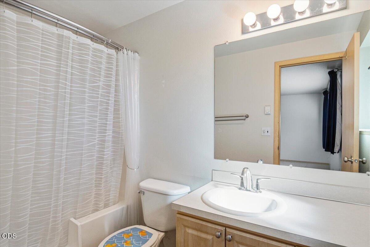 Bathroom with a patterned shower curtain, toilet, and wood vanity beneath a large mirror.