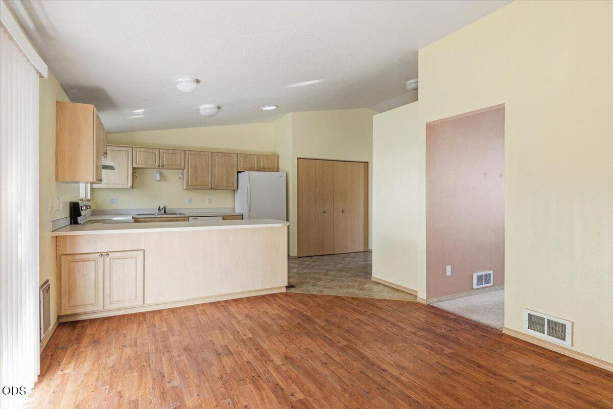 Vacant kitchen with a breakfast bar, light wood cabinets, and wood-look flooring.