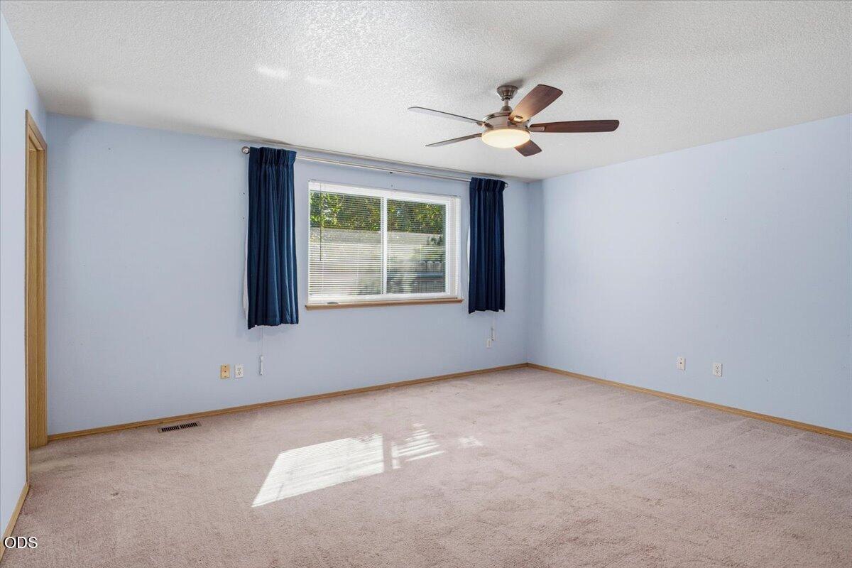 Empty carpeted room with pale blue walls, dark curtains, and a ceiling fan.