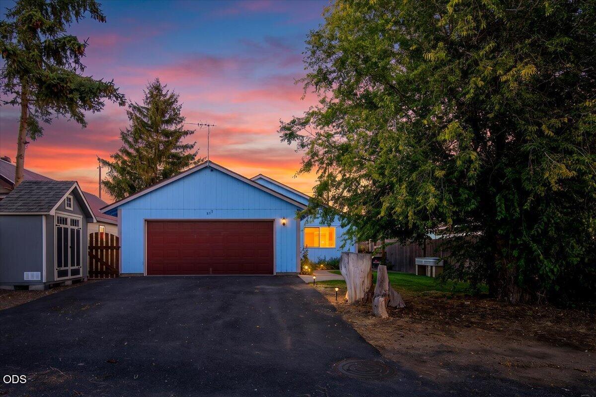 Blue house with a wide red garage door and paved driveway beneath a colorful dusk sky.