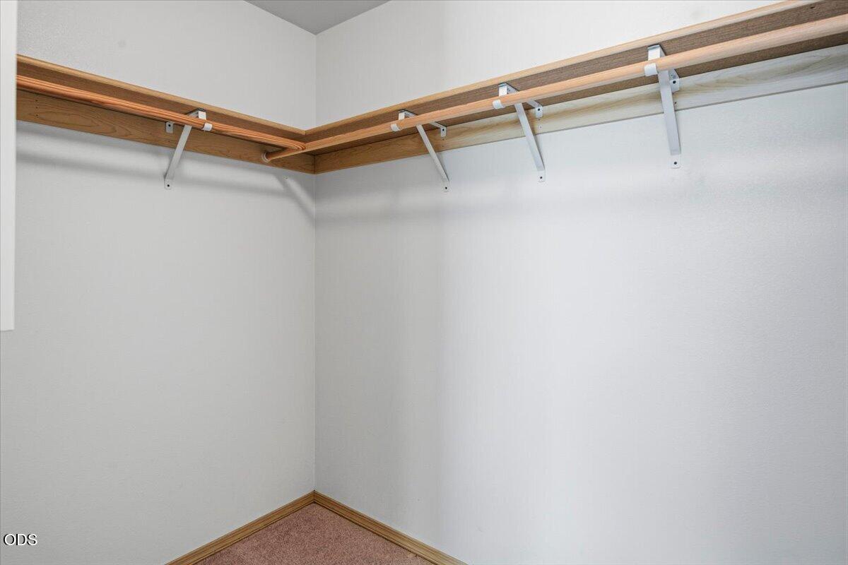 Empty walk-in closet with wraparound wooden shelves and hanging rails.